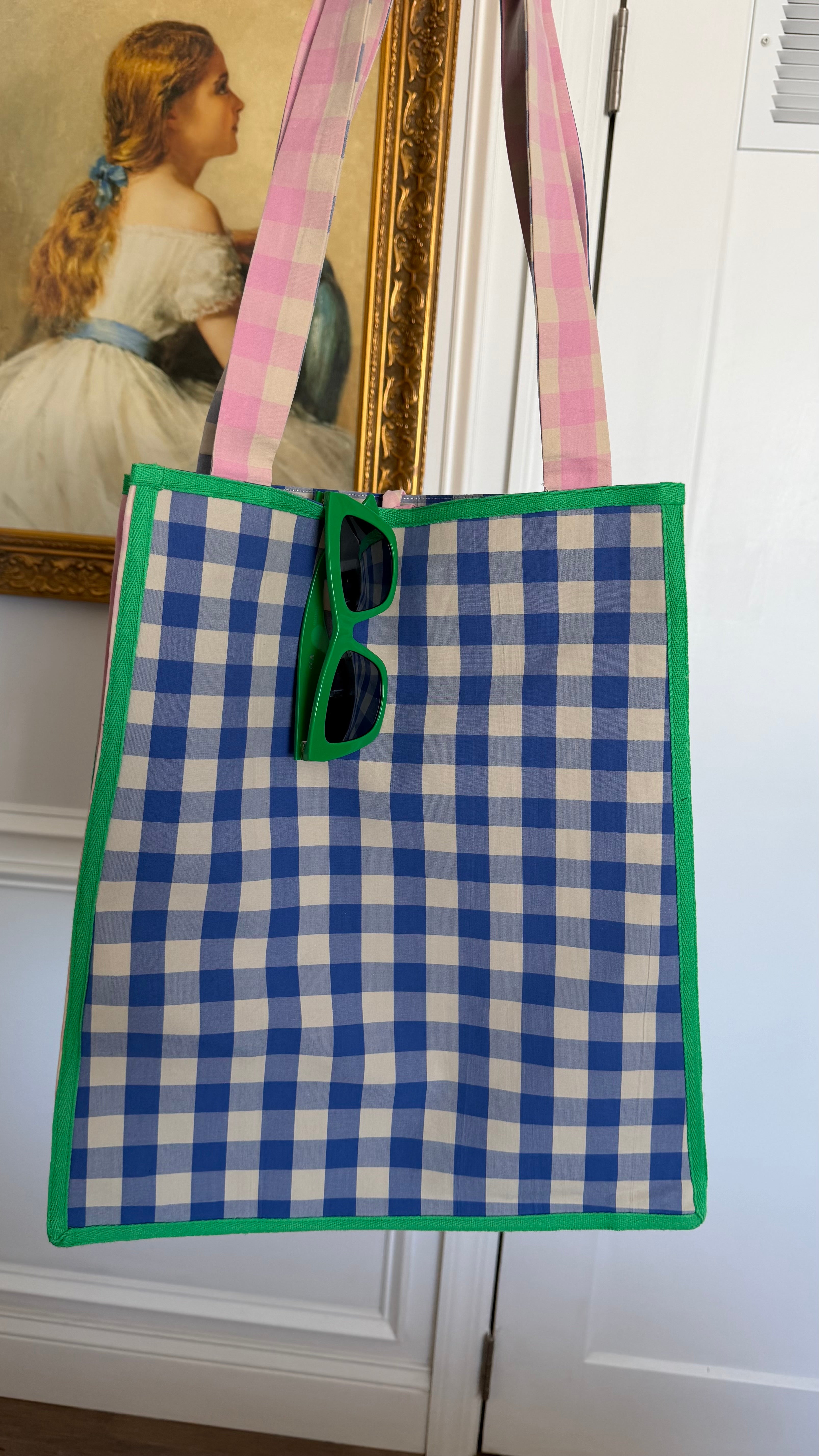 Blue and white checkered bag with green trim hanging on a white door. Maderas Gingham Tote Bag