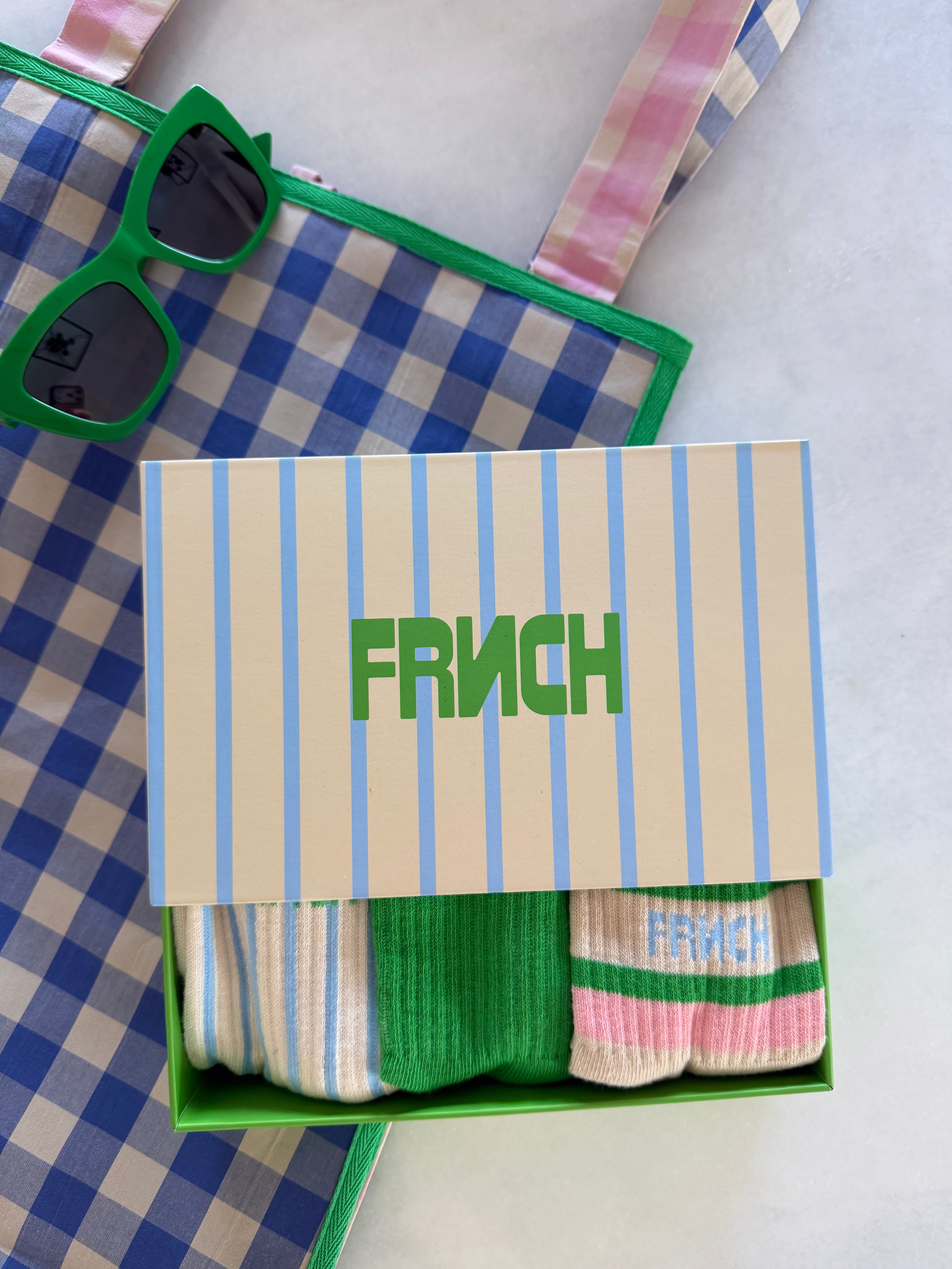 Box of socks with 'FRNCH' branding, sunglasses, and a checkered bag on a light background. FRNCH Tethy Socks Set
