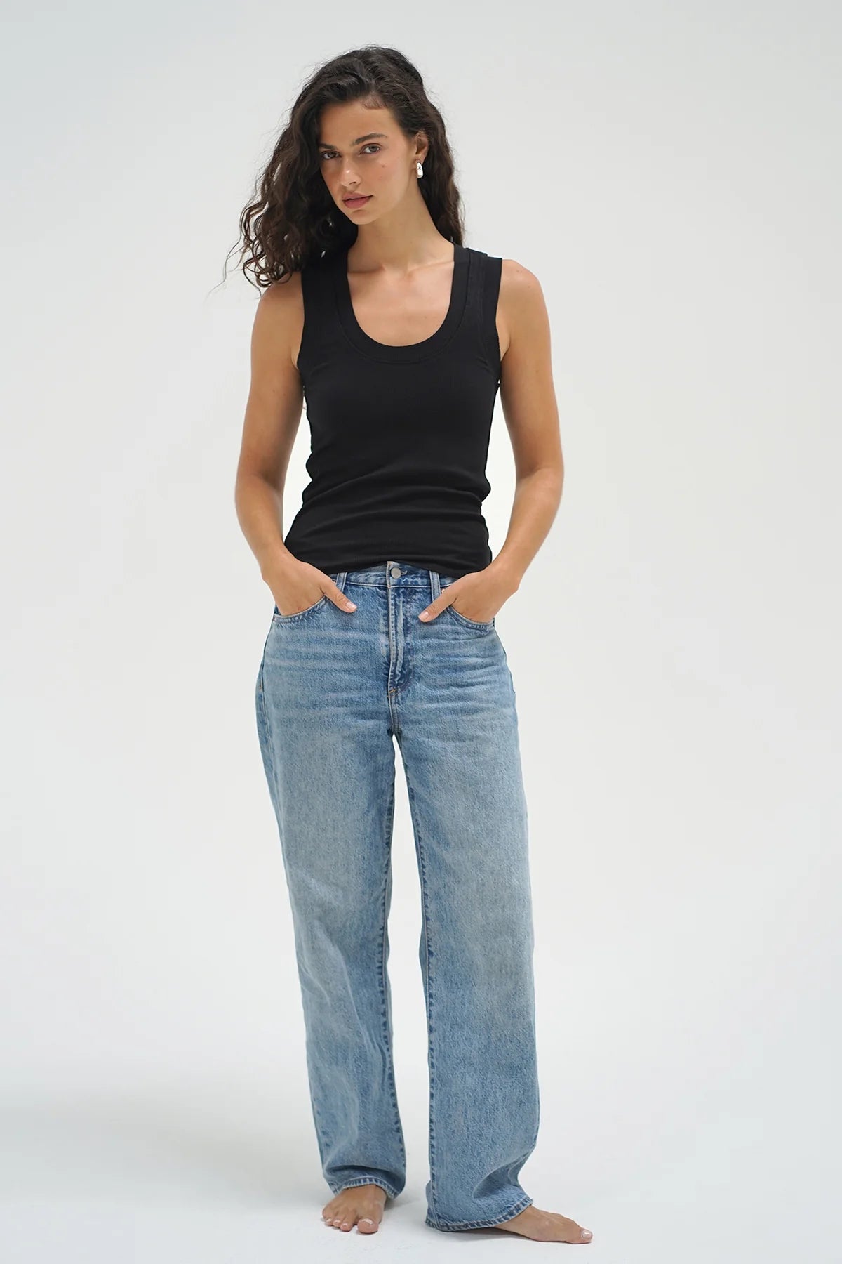 Woman wearing a black tank top and blue jeans on a white background. Woman wearing a white tank top and blue jeans against a plain background. LNA Double Layer Ribbed Scoop Tank at Coco Kimono Boutique