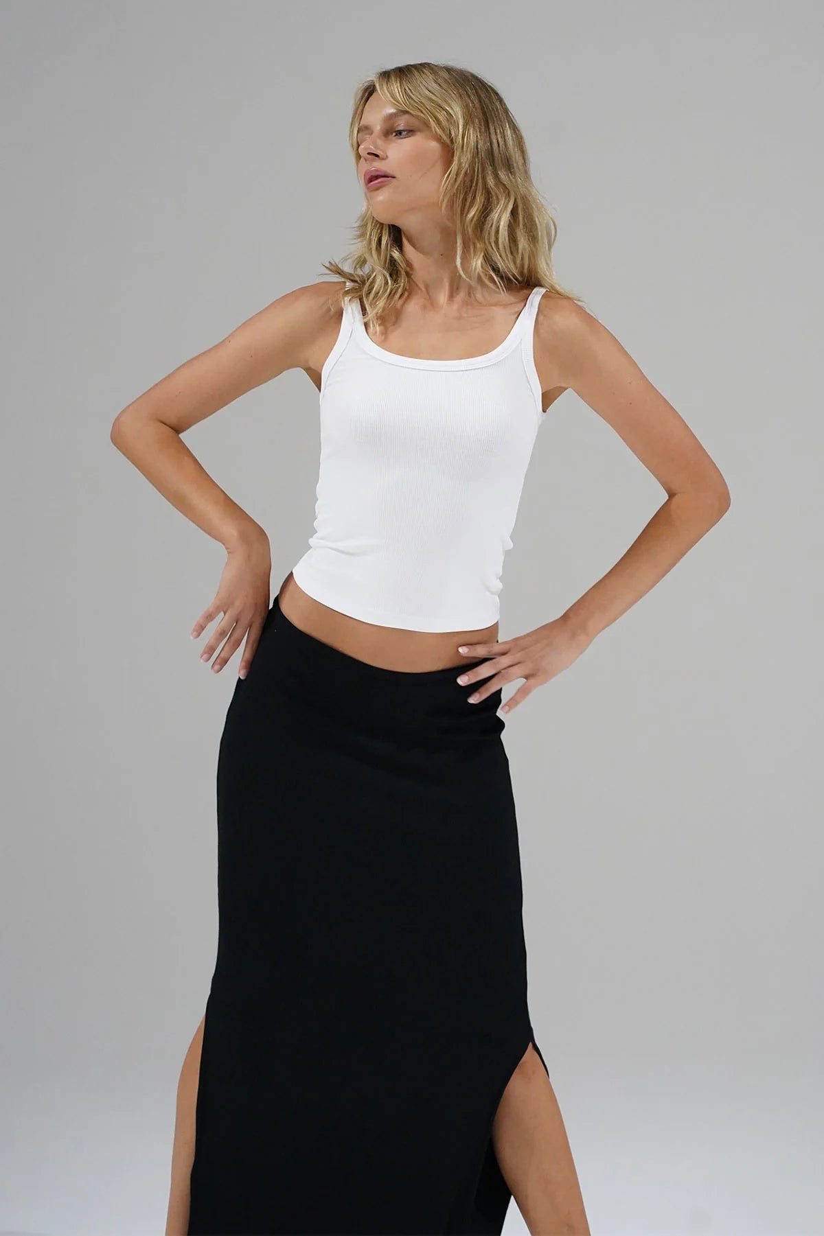 Woman wearing a white tank top and black skirt on a gray background. LNA Timeless Ribbed Tank at Coco Kimono