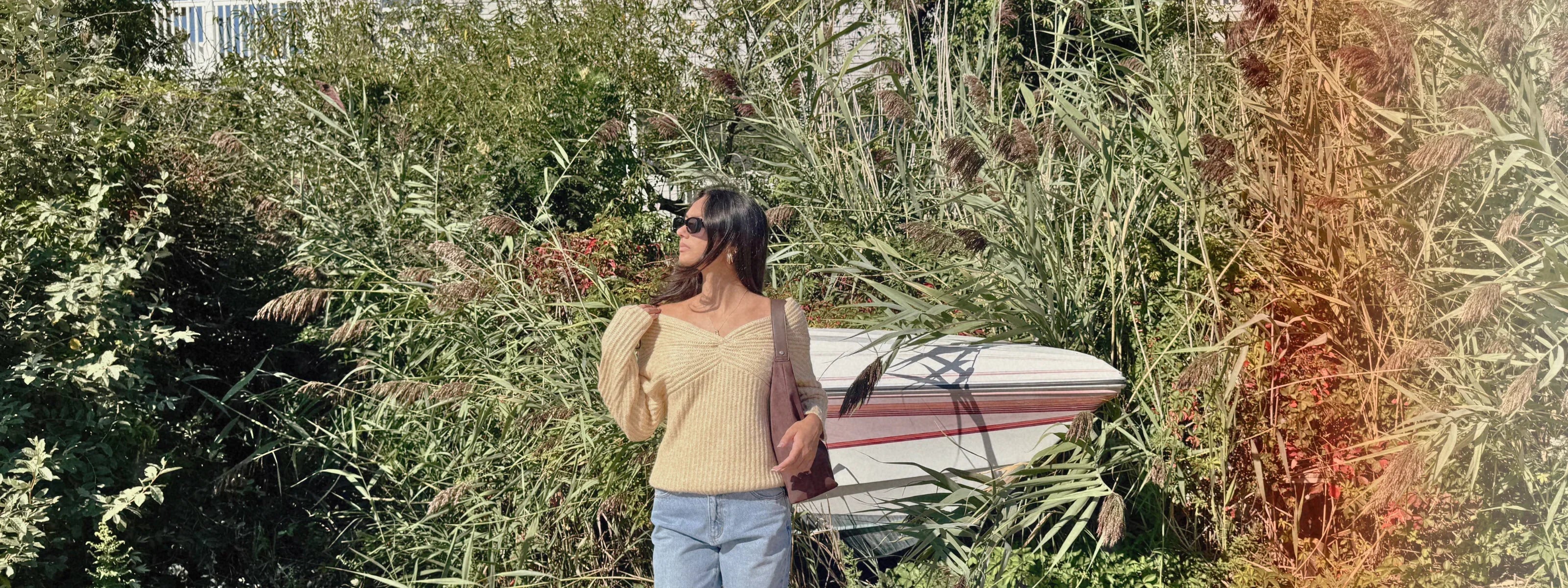 yellow sweater and jeans with boat in the back popping out of the grass