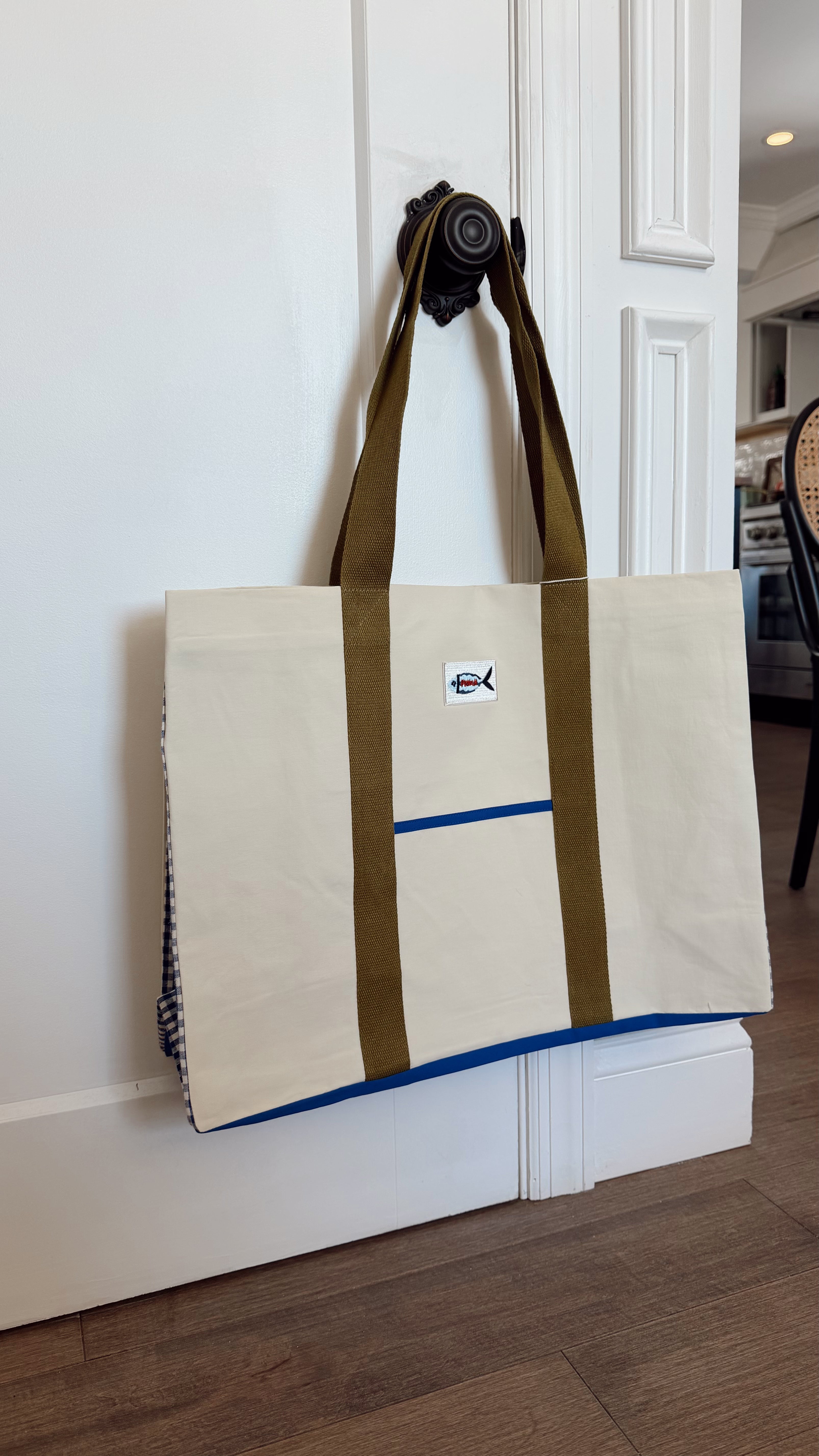 FRNCH Lyra Tote Bag. Beige tote bag with brown straps hanging on a white door