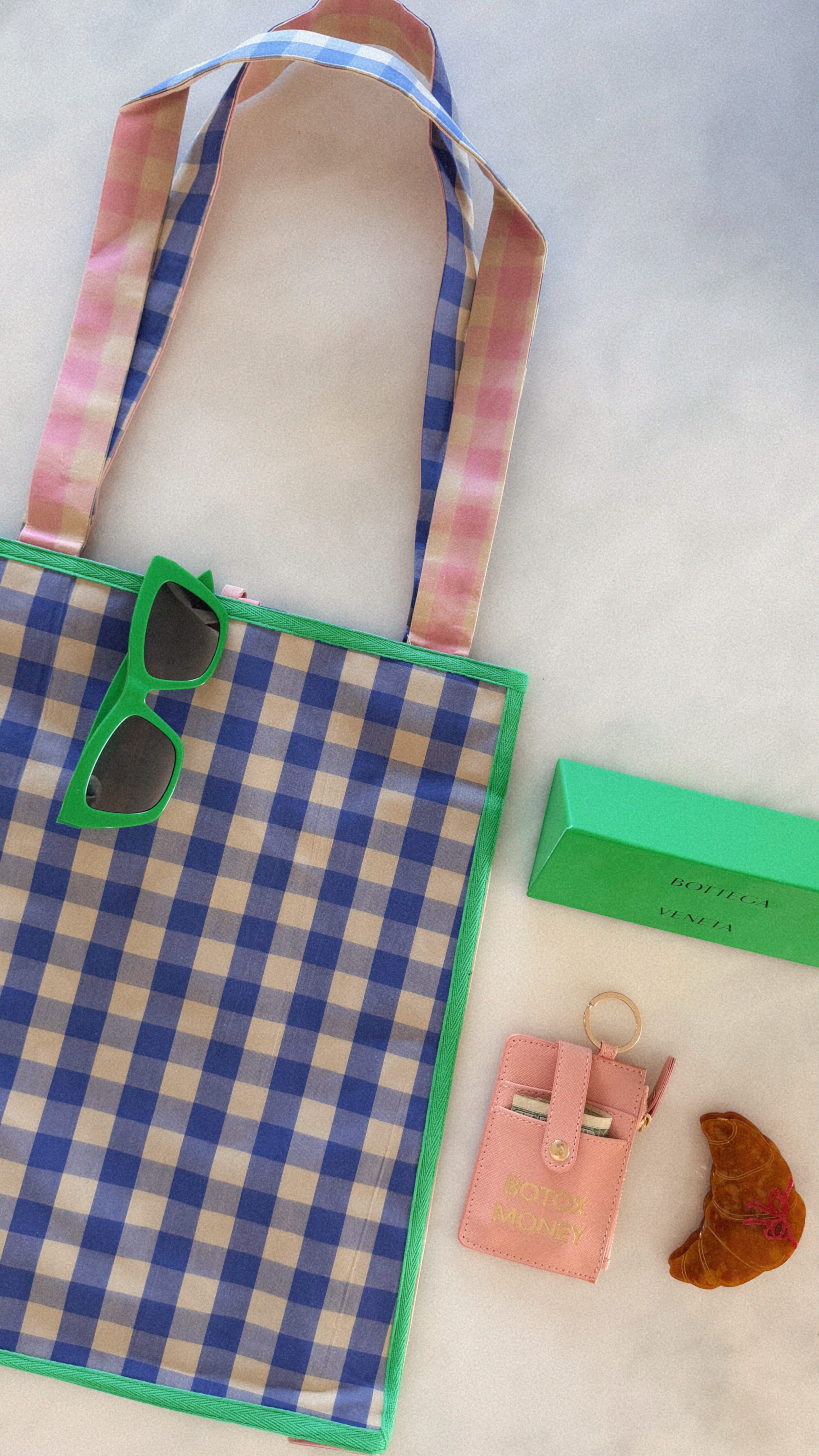 Plaid bag with sunglasses, green box, pink wallet, and brown leaf on a white background. Maderas Gingham Tote Bag