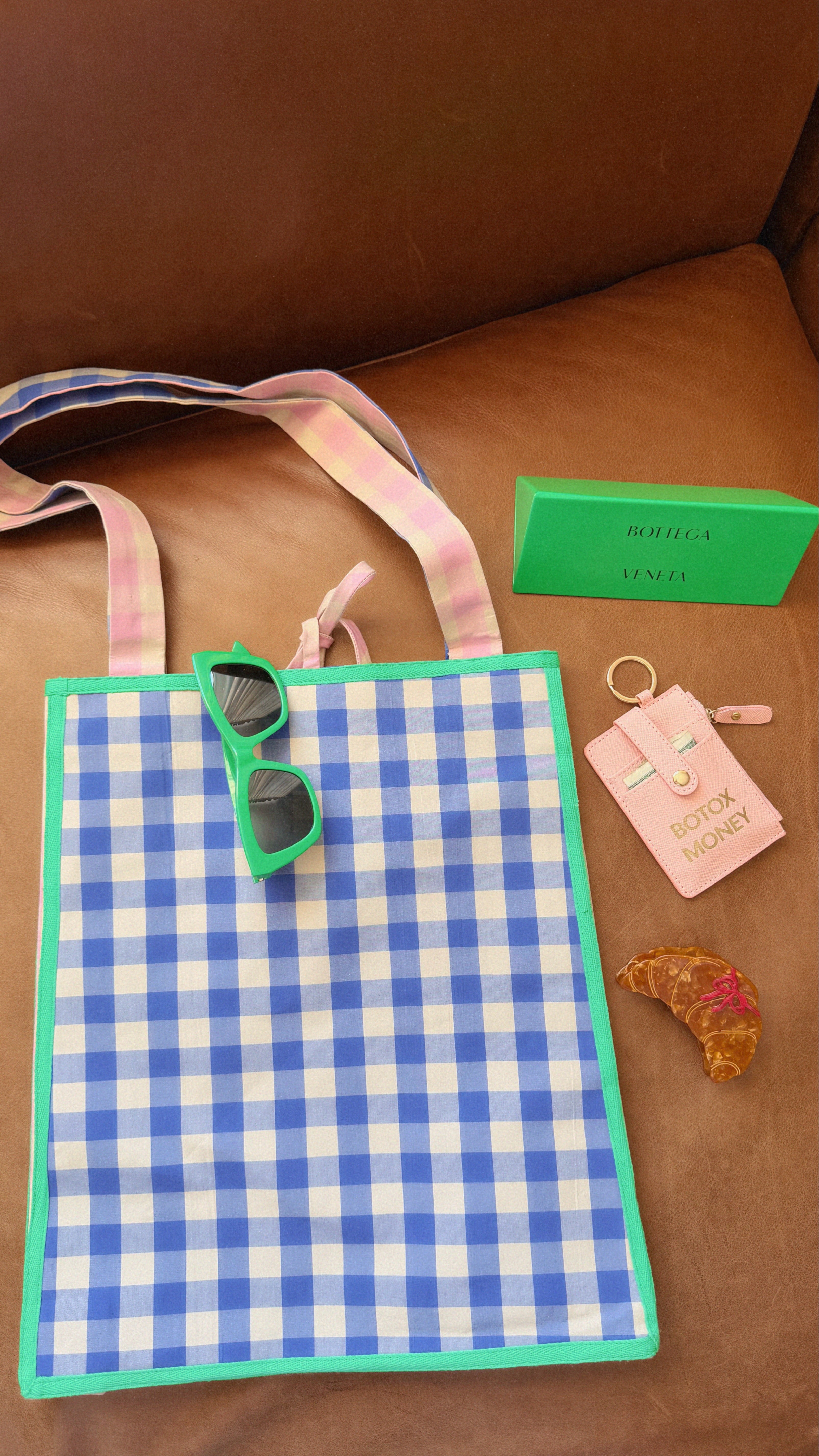 Blue and white checkered bag with sunglasses, keychain, and green box on a brown surface. Maderas Gingham Tote Bag