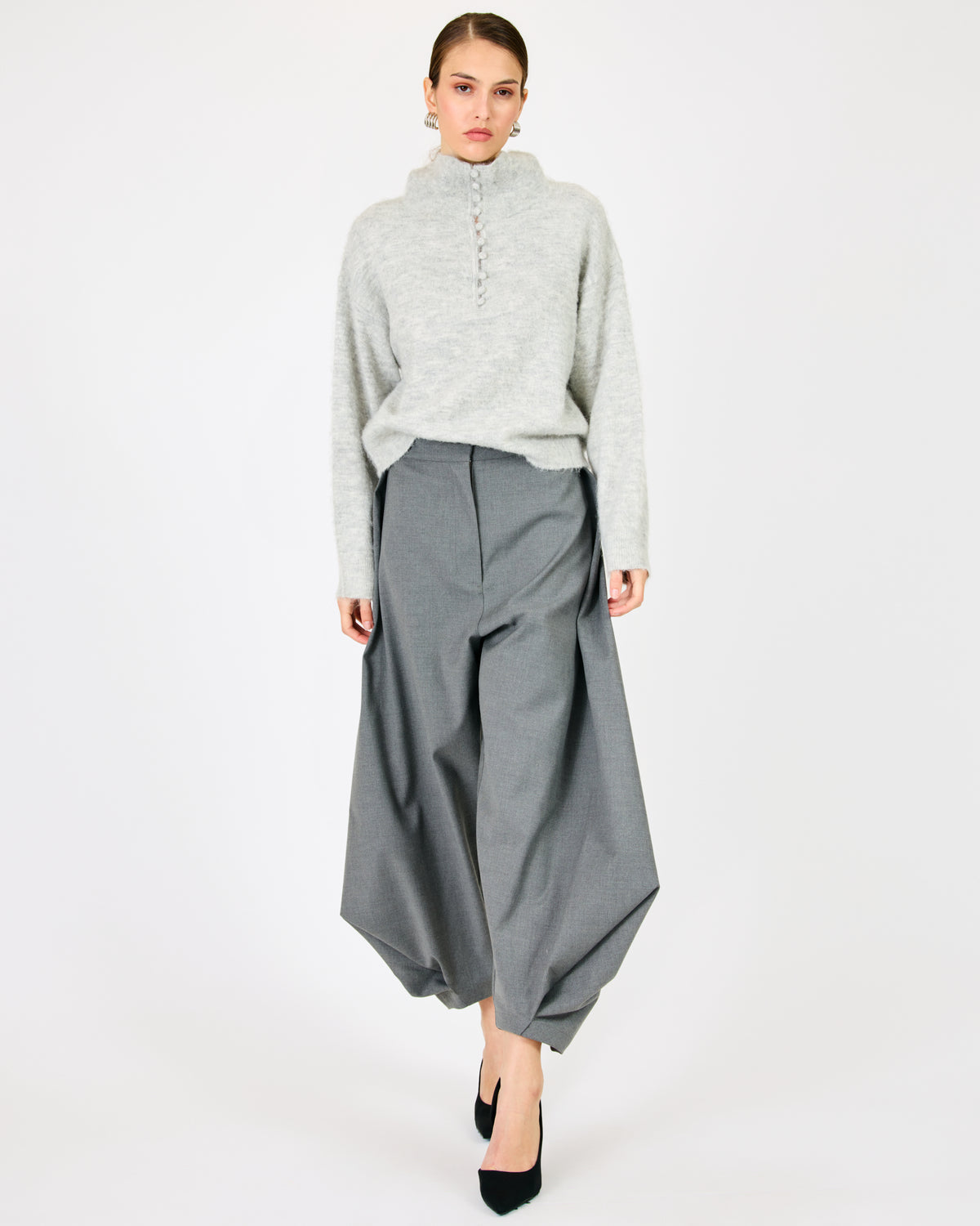 A model wearing a light gray mock-neck knit sweater and wide-leg gray trousers, paired with black heels, against a plain white studio background.

Line and Dot Maelly Sweater in Gray worn by model - Coco Kimono Boutique LBI