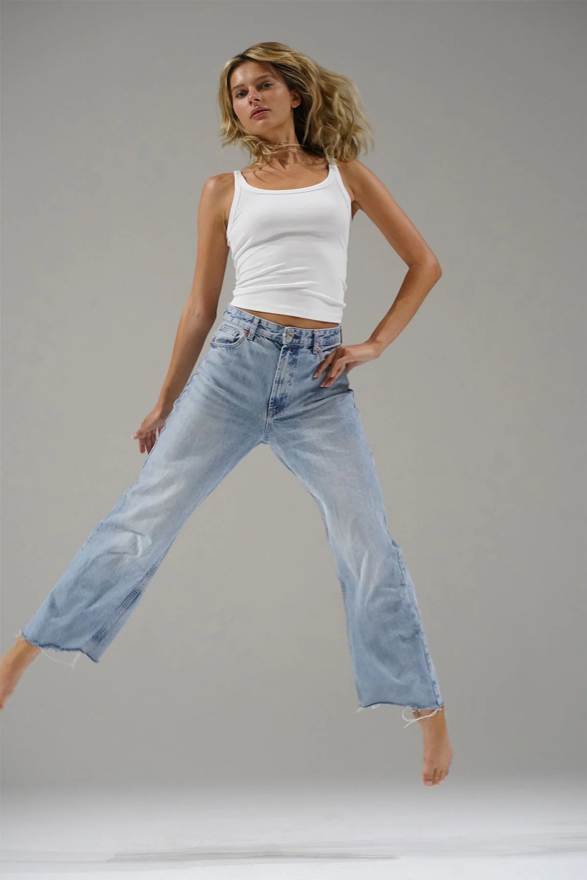 Woman wearing a white tank top and blue jeans against a gray background. LNA Timeless Ribbed Tank at Coco Kimono 